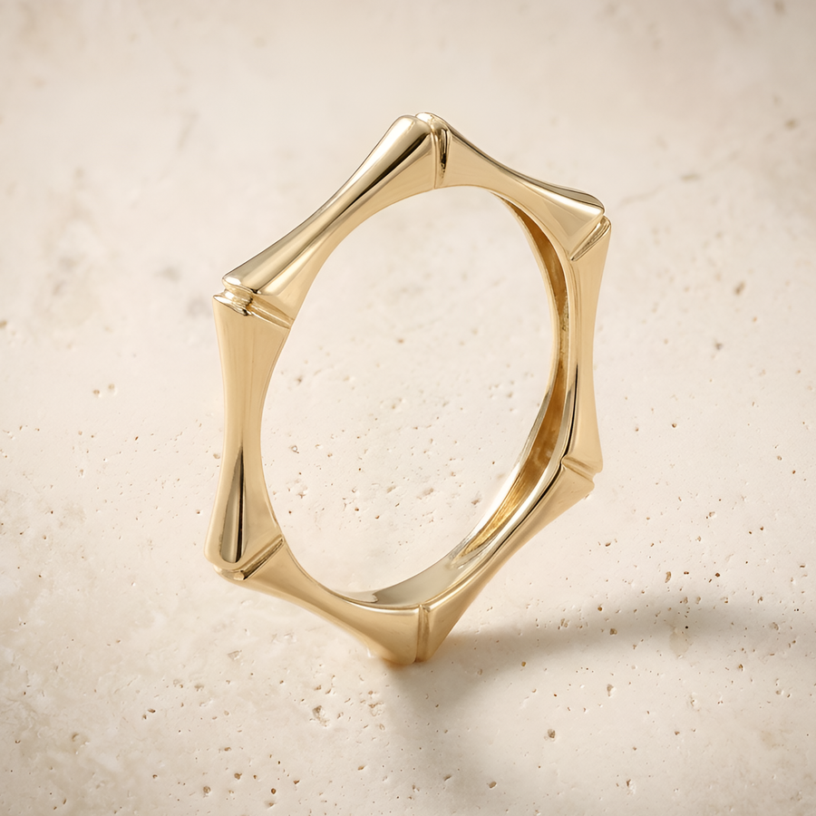 Hexa ring in 14K solid gold, skeletal hexagonal band with flared corners, on cream travertine